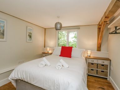 A bedroom with a bed white bedding red pillow two bedside tables lamps window wooden beams at Roman Lodge in Osmington