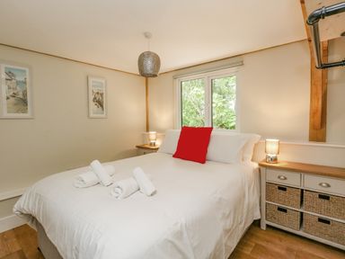 A bedroom with a bed with white bedding and a red pillow two bedside tables with lamps and framed pictures on the wall at Roman Lodge in Osmington