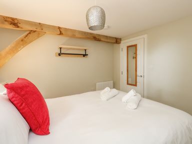A bedroom with a bed with white bedding and a red pillow three rolled white towels wooden beam on the wall and a door with a mirror Roman Lodge Osmington