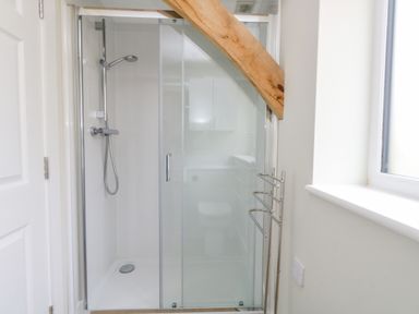 A bathroom with a glass shower enclosure metal towel rack wooden beam and a window at Roman Lodge in Osmington
