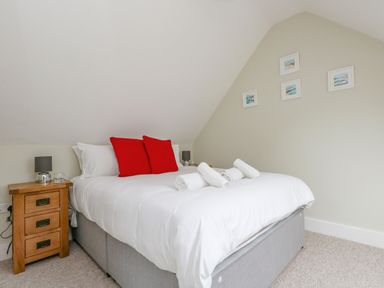 A bedroom with a bed with white bedding red pillows and rolled towels next to wooden bedside tables with lamps and framed pictures on the wall at Roman Lodge in Osmington