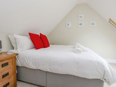 A bedroom with a bed with white bedding and red pillows next to a wooden bedside table with a glass Roman Lodge Osmington