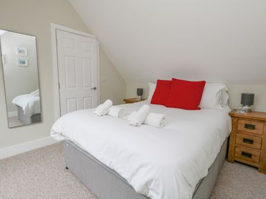 A bedroom with a bed with white bedding and red pillows and wooden bedside tables with lamps at Roman Lodge in Osmington