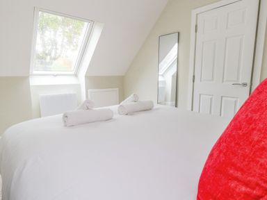 A bedroom with a white bed, three rolled towels, a red pillow, a window, a door, and a wall mirror at Roman Lodge in Osmington