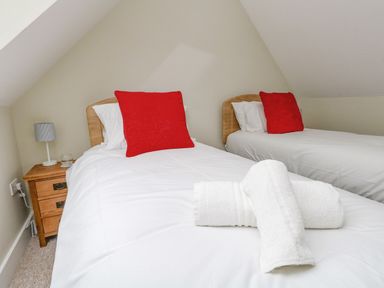 A bedroom with two single beds with red pillows and folded white towels on one bed at Roman Lodge in Osmington
