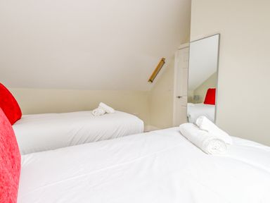 A bedroom with two single beds with white linens red pillows and rolled towels with a wall mirror and door in the background at Roman Lodge in Osmington