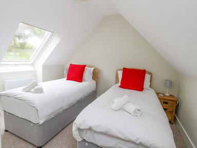 A bedroom with two single beds with white bedding and red pillows and a window on a slanted ceiling at Roman Lodge in Osmington