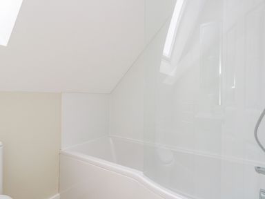 A bathroom with a white bathtub and glass shower screen at Roman Lodge in Osmington