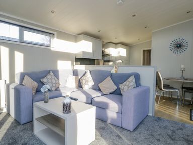 A living room with a blue sofa a white coffee table and a dining area with chairs at Yealand 36 in Tewitfield