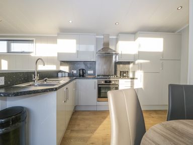 A kitchen with grey cabinets black countertops a stainless steel oven and stove a sink and dining chairs at Yealand 36 in Tewitfield