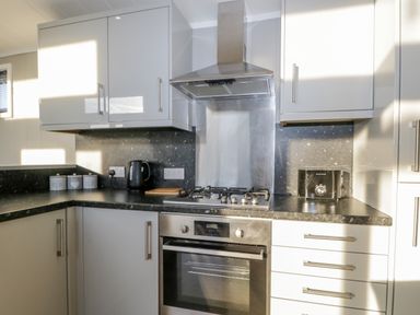 A kitchen with a gas stove oven kettle toaster and storage cabinets at Yealand 36 in Tewitfield