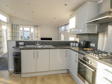 A kitchen with white cabinets a gas stove oven a black kettle a sink and a trash bin at Yealand 36 in Tewitfield