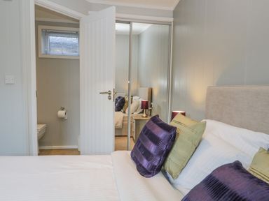 A bedroom with a bed and purple and green pillows next to a mirrored wardrobe and an open door showing a bathroom at Yealand 36 in Tewitfield