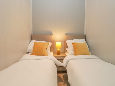 A bedroom with two single beds with white bedding and a yellow pillow on each with a lamp on a bedside table in between at Yealand 36 in Tewitfield