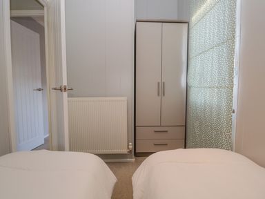 A bedroom with two single beds a wardrobe a radiator and a window with a patterned blind at Yealand 36 in Tewitfield