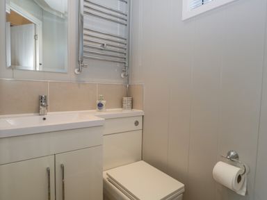 A bathroom with a sink, mirror, towel radiator, toilet, and toilet paper holder at Yealand 36 in Tewitfield