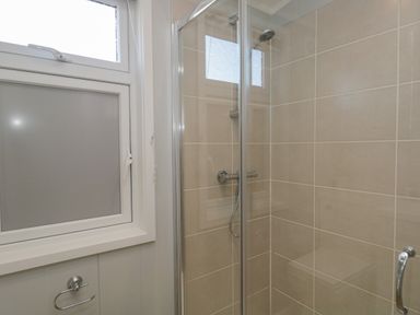 A shower area with tiled walls and a glass door next to a window with frosted glass at Yealand 36 in Tewitfield