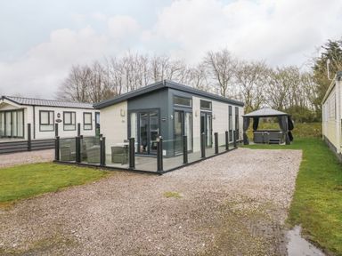 A modern single-story cabin with glass patio fencing and a gazebo with seating at Yealand 36 in Tewitfield