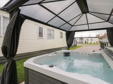 An outdoor hot tub with water under a gazebo next to a white mobile home at Yealand 36 in Tewitfield