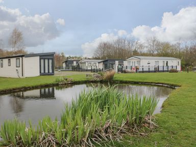 A small pond with plants around it and several mobile homes on grassy land at Yealand 36 in Tewitfield