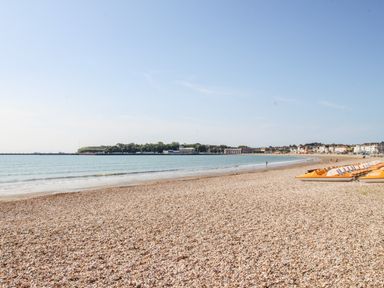A pebble beach with calm sea and boats lined up near the shore at Portside in Greenhill Weymouth
