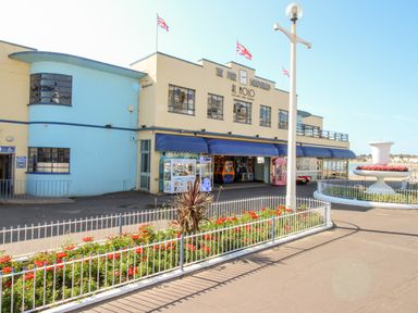 A building with a restaurant and arcade machines outside flowers in fenced garden and Union Jack flags flying near the seafront at Portside Greenhill Weymouth