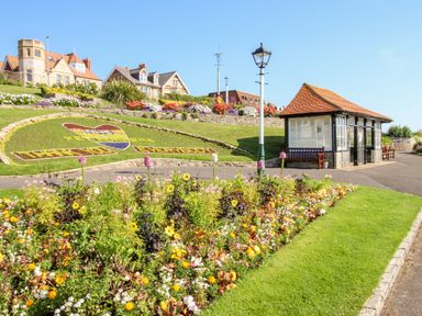 A garden with flowers and a landscaped grassy area with houses and a small pavilion in the background at Portside Greenhill Weymouth
