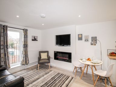A living room with a black leather sofa striped rug armchair wall-mounted TV and a small dining table with white chairs at Portside in Greenhill Weymouth