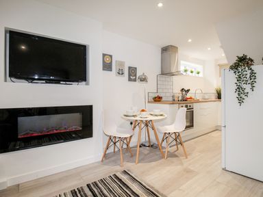 A kitchen and dining area with a mounted television, electric fireplace, round table with two chairs, and kitchen appliances at Portside Greenhill Weymouth