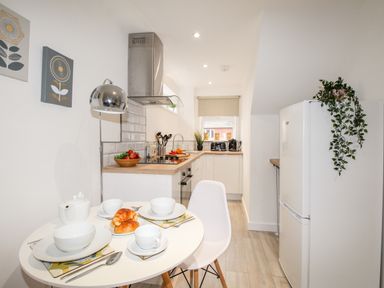A kitchen with a dining table set with croissants dishes and cutlery a fridge with a plant and kitchen appliances and utensils at Portside Greenhill Weymouth