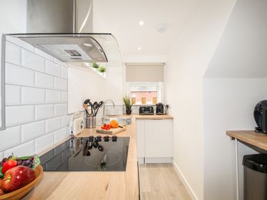 A narrow kitchen with wooden countertops, a stovetop, utensils, toaster, kettle, and a window at Portside in Greenhill Weymouth