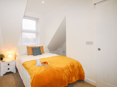 A bedroom with a bed covered with an orange blanket and pillows next to a bedside table with a lamp at Portside in Greenhill Weymouth