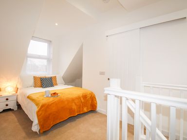 A bedroom with a bed with orange and blue pillows and an orange blanket next to a white bedside table and a staircase in Portside Greenhill Weymouth