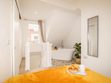 A bathroom with a freestanding bathtub and a plant beside it overlooking a stairwell and a window with curtains at Portside Greenhill Weymouth