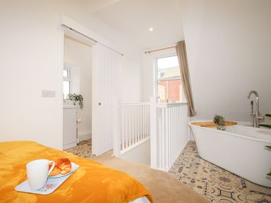 A bathroom with a bathtub near a window and a sliding door leading to a small sink area at Portside in Greenhill Weymouth