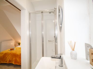 A bathroom with a shower next to a bedroom with a bed covered in a yellow blanket at Portside Greenhill Weymouth