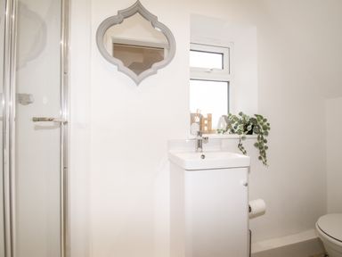 A bathroom with a shower door sink cabinet mounted mirror and window with decorations at Portside Greenhill Weymouth