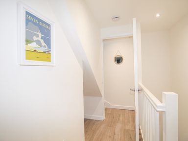A hallway with wooden floor tiles a white door half open a framed picture on the wall and a round mirror on the far wall at Portside Greenhill Weymouth