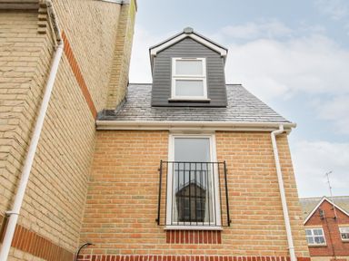 A brick exterior wall with a window and metal railing and a dormer window on the roof at Portside in Greenhill Weymouth