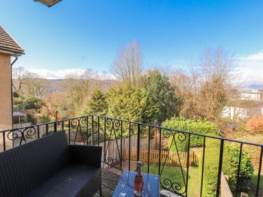 A balcony with a bottle and glasses overlooking a garden at Lake View in Bowness-On-Windermere