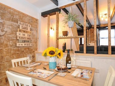 A dining table set with placemats wine glasses a vase of sunflowers and a bottle of wine in a room with wooden beams and a sign on the wall at Walter in Newlyn