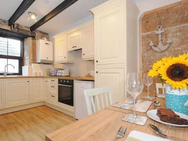 A kitchen with cream cabinets wooden countertops a dining table with glasses sunflower vase and plates with food at Walter in Newlyn