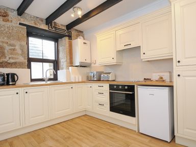 A kitchen with white cabinets wooden countertops a small fridge an oven a toaster a microwave and a kettle at Walter in Newlyn