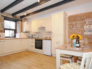 A kitchen with white cabinets and wooden floors and a dining table with sunflowers and wine at Walter in Newlyn