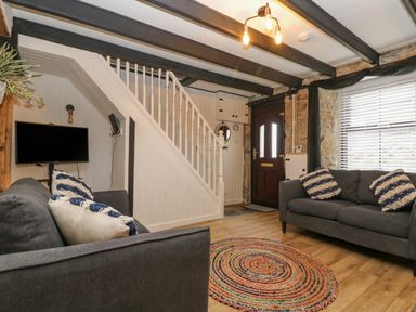A living room with two sofas a round rug a mounted TV stairs and a wooden door at Walter in Newlyn
