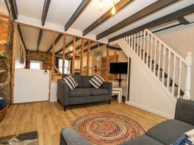 A living room with gray sofas and a colorful round rug near a staircase at Walter in Newlyn