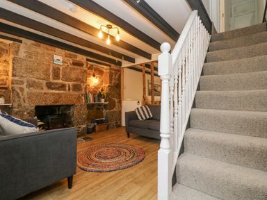 A living room with a stone fireplace two grey sofas a round rug wooden floor and stairs with carpet at Walter in Newlyn