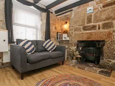A sitting area with a grey sofa and two cushions near a stone fireplace with a stove and a plant at Walter in Newlyn