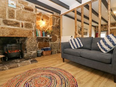 A living room with a grey sofa and blue and white pillows near a stone fireplace and a round colorful rug at Walter in Newlyn