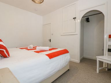 A bedroom with a bed featuring red and white bedding two rolled towels on the bed a white door an arched open closet with hangers and a white chair at Walter in Newlyn